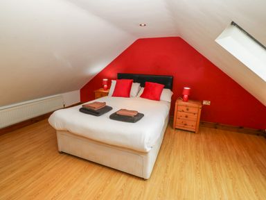 A bedroom with a bed with red pillows and folded towels on top two wooden bedside tables with red lamps a slanted ceiling and a skylight window at Cefn-Yr-Efail Golan near Porthmadog