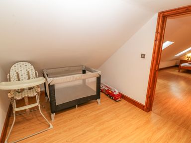 A baby high chair a playpen and a toy fire truck near a doorway leading to a bedroom at Cefn-Yr-Efail in Golan near Porthmadog