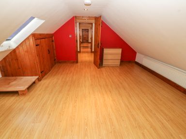 An attic room with wooden flooring a small wooden cabinet a skylight window and a red accent wall at Cefn-Yr-Efail in Golan near Porthmadog