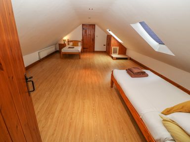 An attic bedroom with two single beds a skylight window a wooden door a bedside table and wooden flooring at Cefn-Yr-Efail in Golan near Porthmadog