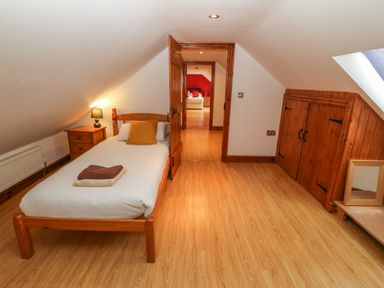 A bedroom with a single bed bedside table and lamp wooden storage and a doorway leading to another bedroom at Cefn-Yr-Efail in Golan near Porthmadog