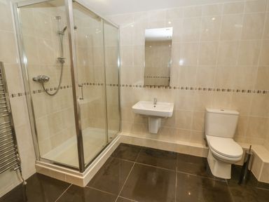 A bathroom with a glass shower enclosure a wall-mounted sink a toilet and tiled walls and floor at Cefn-Yr-Efail in Golan near Porthmadog