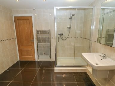 A bathroom with a wooden door a metal heated towel rail a glass shower enclosure and a white wall-mounted sink at Cefn-Yr-Efail in Golan near Porthmadog