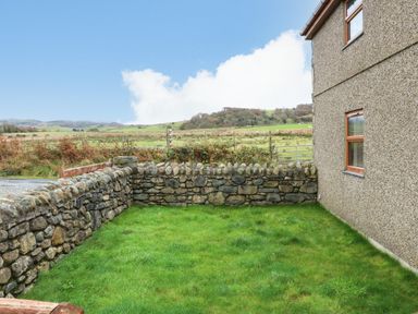 A stone wall enclosing a grassy yard beside a house with countryside fields in the background at Cefn-Yr-Efail in Golan near Porthmadog