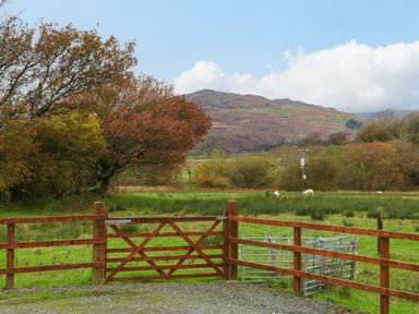 A wooden fence and gate with a grassy field and trees and hills in the background at Cefn-Yr-Efail Golan near Porthmadog