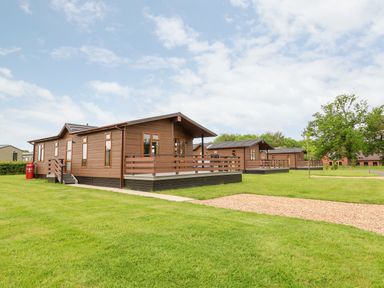 Brown wooden lodges with porches on green lawns under a cloudy sky at Callow Lodge 15 Beaconsfield Farm Holiday Park near Shrewsbury