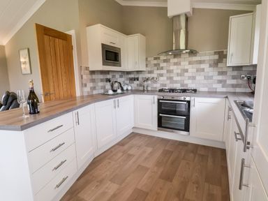 A kitchen with white cabinets a gas stove an oven a microwave and wooden flooring at Callow Lodge 15 Beaconsfield Farm Holiday Park near Shrewsbury