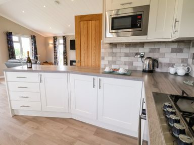 A kitchen with white cabinets wooden countertop microwave kettle and teapot at Callow Lodge 15 Beaconsfield Farm Holiday Park near Shrewsbury