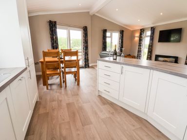 A kitchen and dining area with wooden chairs and table and kitchen island with glasses and bottle at Callow Lodge 15 at Beaconsfield Farm Holiday Park near Shrewsbury