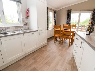 A kitchen and dining area with white cabinets wooden dining table chairs and a bottle with glasses at Callow Lodge 15 Beaconsfield Farm Holiday Park near Shrewsbury