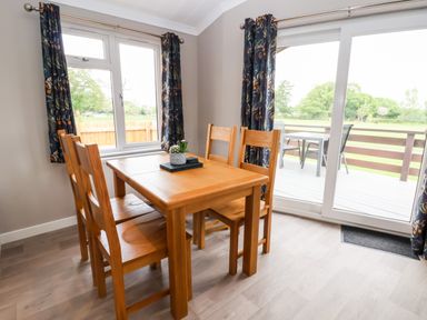 A dining area with a wooden table and four chairs near windows and sliding glass doors at Callow Lodge 15 Beaconsfield Farm Holiday Park near Shrewsbury