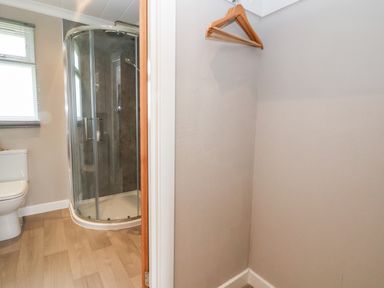 A bathroom with a shower enclosure and toilet and an adjacent small space with wooden hangers on the wall at Callow Lodge 15 Beaconsfield Farm Holiday Park near Shrewsbury