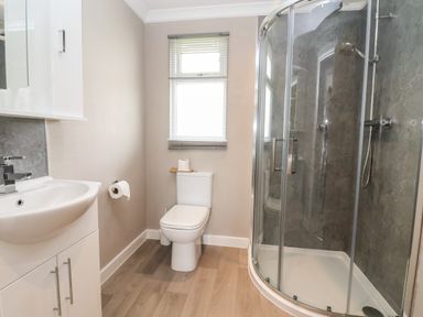A bathroom with a corner shower, toilet, sink with cabinet, and window blinds at Callow Lodge 15 Beaconsfield Farm Holiday Park near Shrewsbury