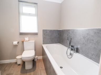 A bathroom with a toilet next to a bathtub with grey tiled walls at Callow Lodge 15 Beaconsfield Farm Holiday Park near Shrewsbury