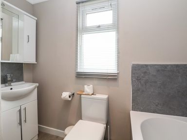 A bathroom with a white sink cabinet mirror a toilet under a window and a bathtub with gray tile wall at Callow Lodge 15 Beaconsfield Farm Holiday Park near Shrewsbury