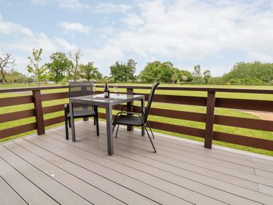 An outdoor patio with a table holding a bottle and two glasses and two chairs at Callow Lodge 15 Beaconsfield Farm Holiday Park near Shrewsbury