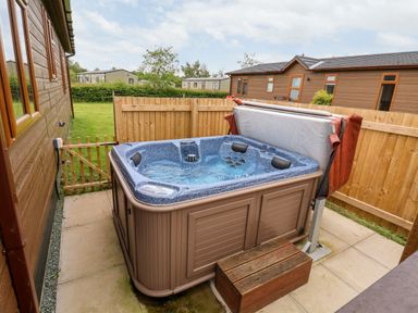 An outdoor hot tub beside a wooden cabin with a wooden fence and lawn in the background at Callow Lodge 15 Beaconsfield Farm Holiday Park near Shrewsbury