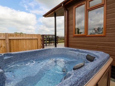 An outdoor hot tub next to a brown wooden building with a window and a fenced patio area at Callow Lodge 15 Beaconsfield Farm Holiday Park near Shrewsbury