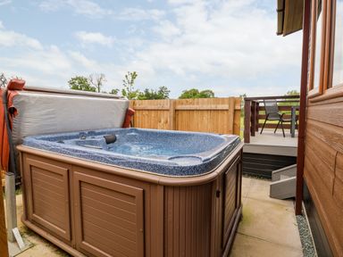 An outdoor hot tub next to a wooden fence and a patio with a table and chairs at Callow Lodge 15 Beaconsfield Farm Holiday Park near Shrewsbury