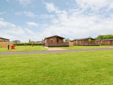 A green lawn with several brown wooden lodges along a paved path at Callow Lodge 15 Beaconsfield Farm Holiday Park near Shrewsbury