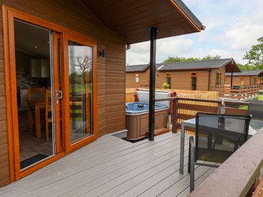 A patio with glass door leading to dining area and a hot tub next to a table with chairs at Callow Lodge 15 Beaconsfield Farm Holiday Park near Shrewsbury