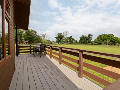 A wooden deck with table and chairs overlooking a grassy field with trees at Callow Lodge 15 Beaconsfield Farm Holiday Park near Shrewsbury