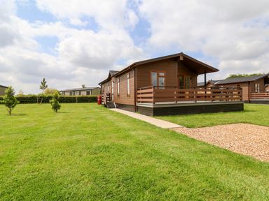 A wooden lodge with a deck and railing on a grassy lawn with small trees at Callow Lodge 15 Beaconsfield Farm Holiday Park near Shrewsbury