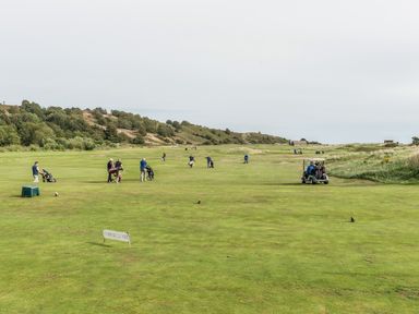 A golf course with players walking and a golf cart on the grass at Jackson Cottage in Alnmouth