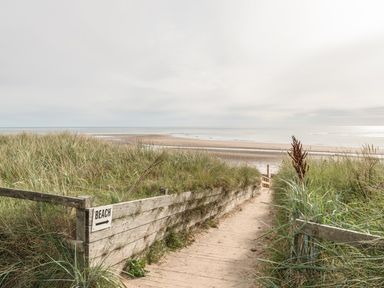 A sandy path leading to the beach with grass and wooden fencing at Jackson Cottage in Alnmouth