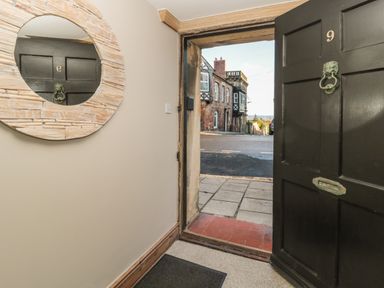 An open black front door with a round wall mirror reflecting a door opposite at Jackson Cottage in Alnmouth
