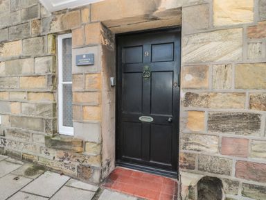 A black front door with the number 9 on a stone wall with a small window to the left at Jackson Cottage in Alnmouth