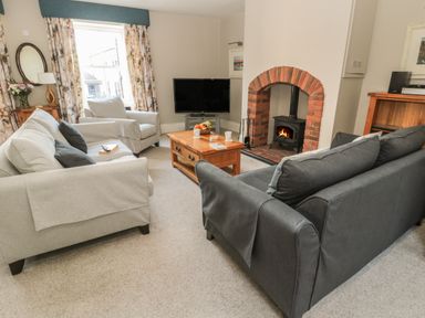 A living room with a gray sofa and armchair a wooden coffee table a television and a wood burning stove at Jackson Cottage in Alnmouth