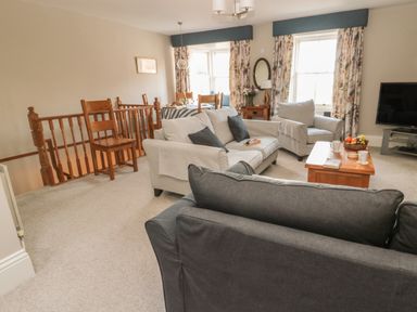 A living room with sofas a coffee table a television dining table and wooden staircase at Jackson Cottage in Alnmouth