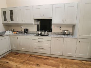 A kitchen with white cabinets, marble countertops, a black kettle, toaster, pots on the stove, and wooden floor at Jackson Cottage in Alnmouth