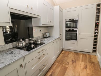 A kitchen with white cabinets stainless steel pots on a stovetop built in ovens and a wine rack at Jackson Cottage in Alnmouth