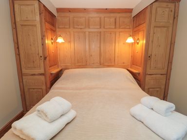 A bedroom with a double bed two folded towels on the bed wooden paneling and two wall lamps at Jackson Cottage in Alnmouth