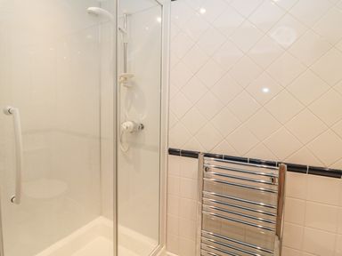 A shower area with glass door and towel radiator on tiled wall at Jackson Cottage in Alnmouth