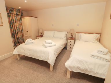 A bedroom with two beds bedside tables lamps a wardrobe and floral curtains at Jackson Cottage in Alnmouth