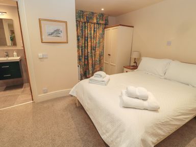 A bedroom with a double bed and folded towels on it a wardrobe with a side table and lamp and patterned curtains at Jackson Cottage in Alnmouth