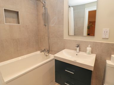 A bathroom with a bathtub a shower a sink with a cabinet and a mirror at Jackson Cottage in Alnmouth