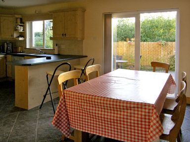 A kitchen and dining area with a checkered tablecloth on the table and sliding glass doors opening to a garden at 19 River Glen in Curracloe County Wexford