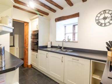 A kitchen with white cabinets black countertops a double oven a sink under a window and exposed wooden beams at Isallt Llanfair near Harlech
