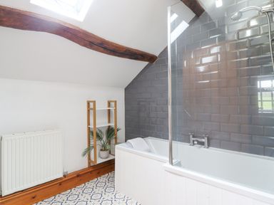 A bathroom with a bathtub with gray tiles on the wall a white wooden shelf with a plant and patterned floor tiles at Isallt in Llanfair near Harlech