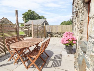 An outdoor patio with wooden table and chairs pink flowers in a pot stone walls and fences at Isallt in Llanfair near Harlech