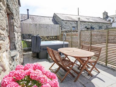 An outdoor patio with a wooden table and chairs a hot tub and a pink flower bush at Isallt Llanfair near Harlech
