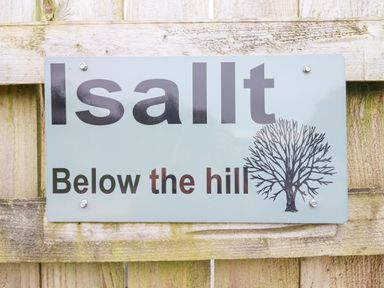 A sign on a wooden fence displaying the words Isallt Below the hill with a tree illustration at Isallt Llanfair near Harlech
