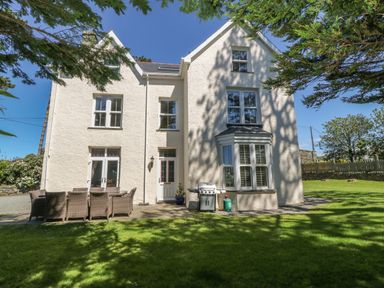 A white two-story house with multiple windows patio furniture and a barbecue on a lawn at Tyddyn Goronwy in Talybont