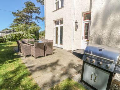 An outdoor patio with a dining table and chairs next to a barbecue grill at Tyddyn Goronwy in Talybont