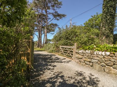 A gravel path with wooden gates stone wall and trees at Tyddyn Goronwy in Talybont