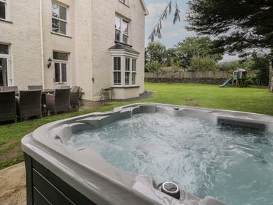 An outdoor hot tub with bubbling water next to a house with a garden and patio furniture at Tyddyn Goronwy in Talybont
